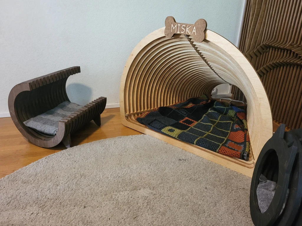 Kirkas-käsitelty koivuvanerinen koirakoti MISKA-luunimikyltillä ja viltillä, vieressä Avoin Lounge.
